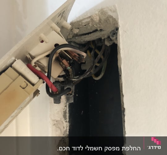 חוטי חשמל חשופים בקופסת חיבורים בקיר
